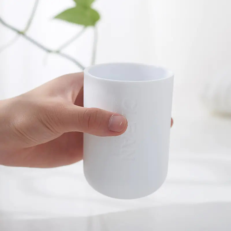 Hand holding a white cup from a bamboo toothbrush holder set on a bright background