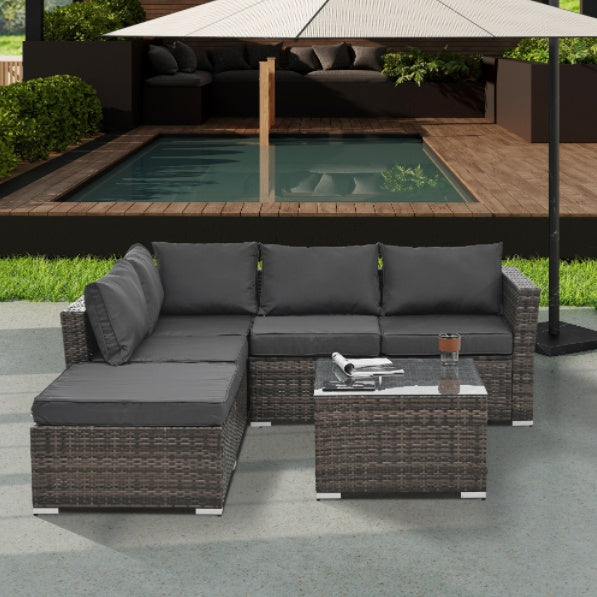 Outdoor wicker patio furniture set with gray cushions and glass coffee table on patio near pool