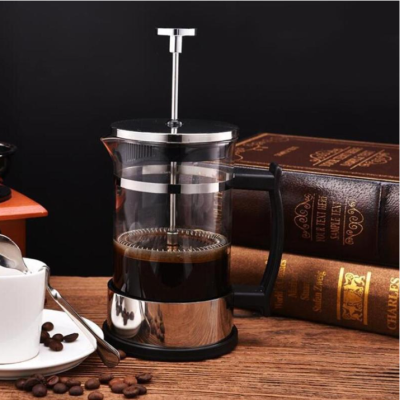 Modern barware accessories including a French press coffee maker on wooden table with coffee beans and books