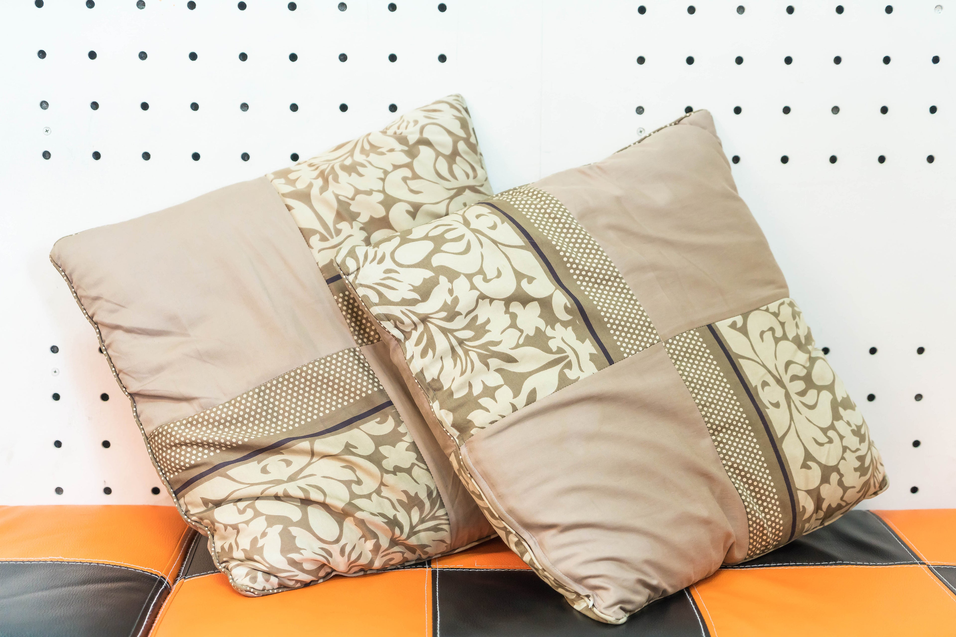 Pair of modern pillow covers for living room in beige and cream patchwork pattern on orange and black couch