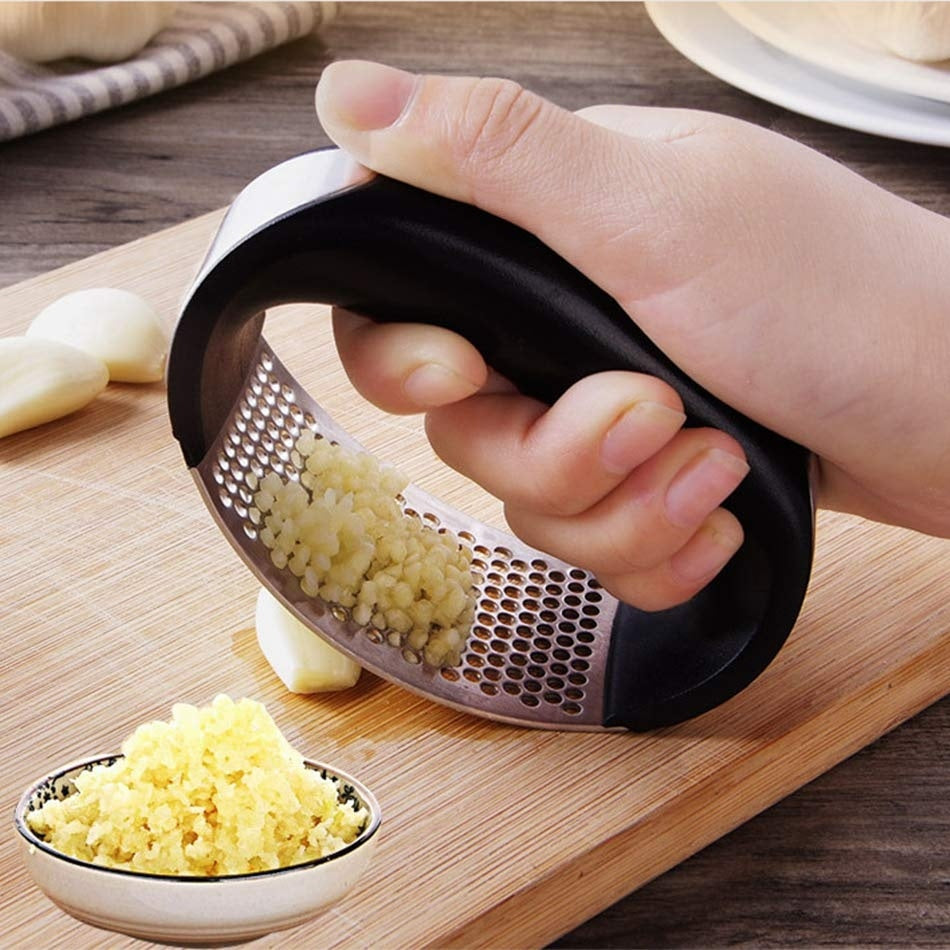 Hand using Shopi Vella stainless steel garlic press to crush garlic on wooden cutting board