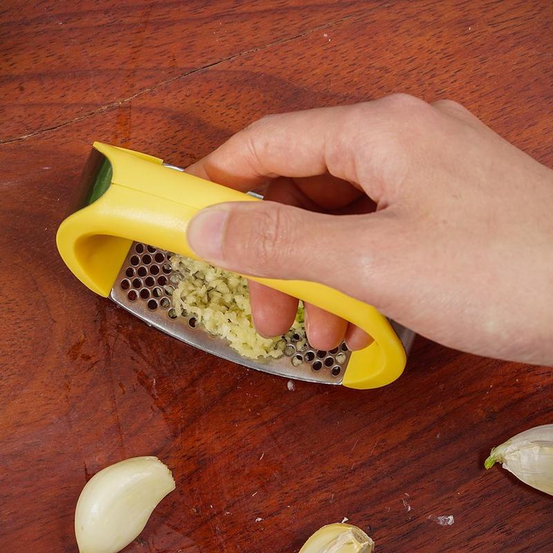 Shopi Vella stainless steel garlic press grating fresh garlic on wooden surface with cloves around
