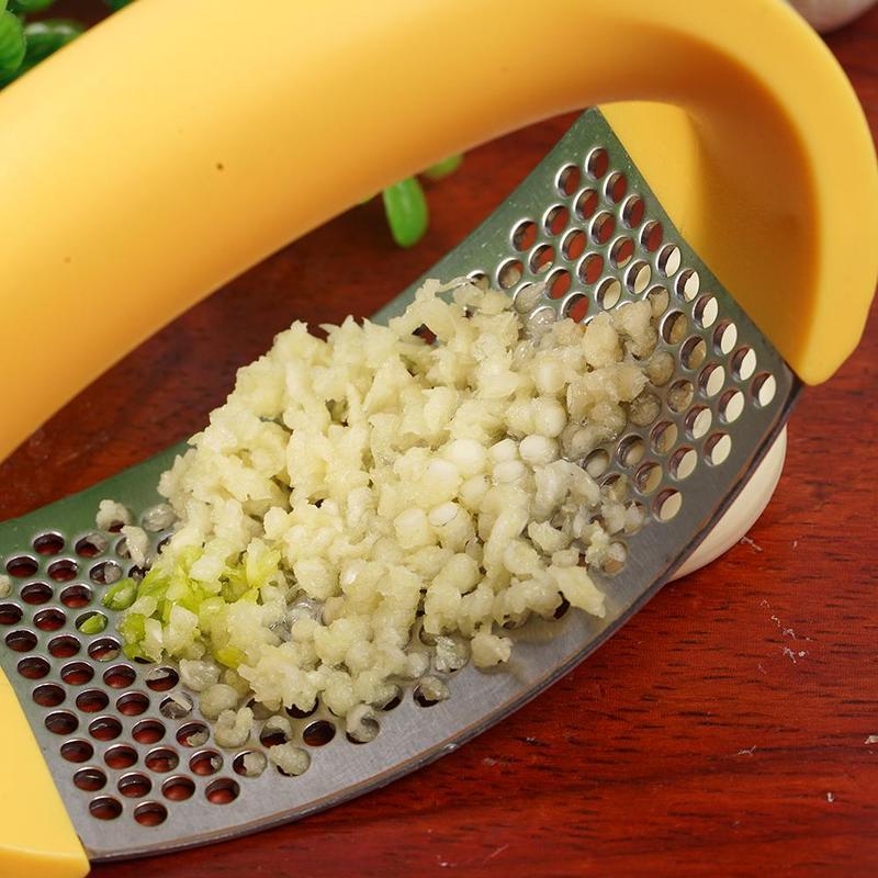Stainless steel garlic press with yellow handle crushing fresh garlic on wooden surface