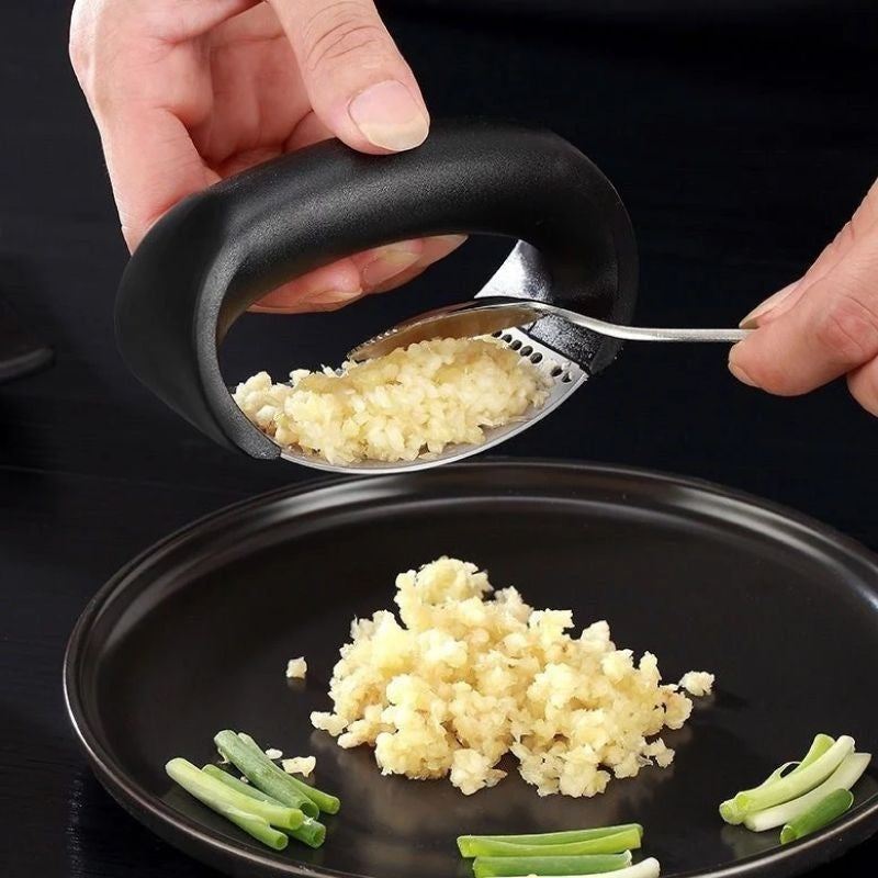 Shopi Vella stainless steel garlic press with ergonomic black handle pressing garlic onto a black plate