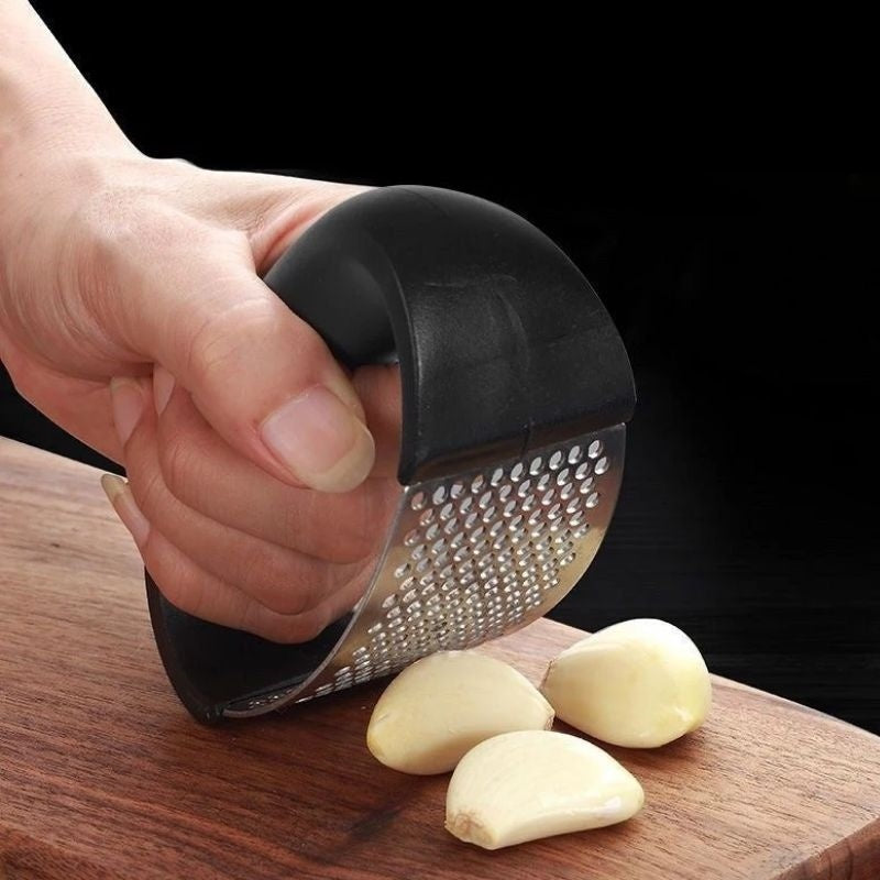 Shopi Vella stainless steel garlic press with ergonomic black handle pressing garlic cloves on wooden board
