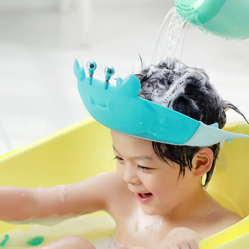 Toddler wearing an adjustable baby shower cap shaped like a blue crab while bathing in a yellow tub