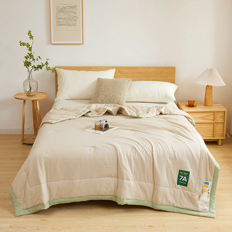 Shopi Vella antibacterial summer quilt in beige with green trim displayed on a wooden bed