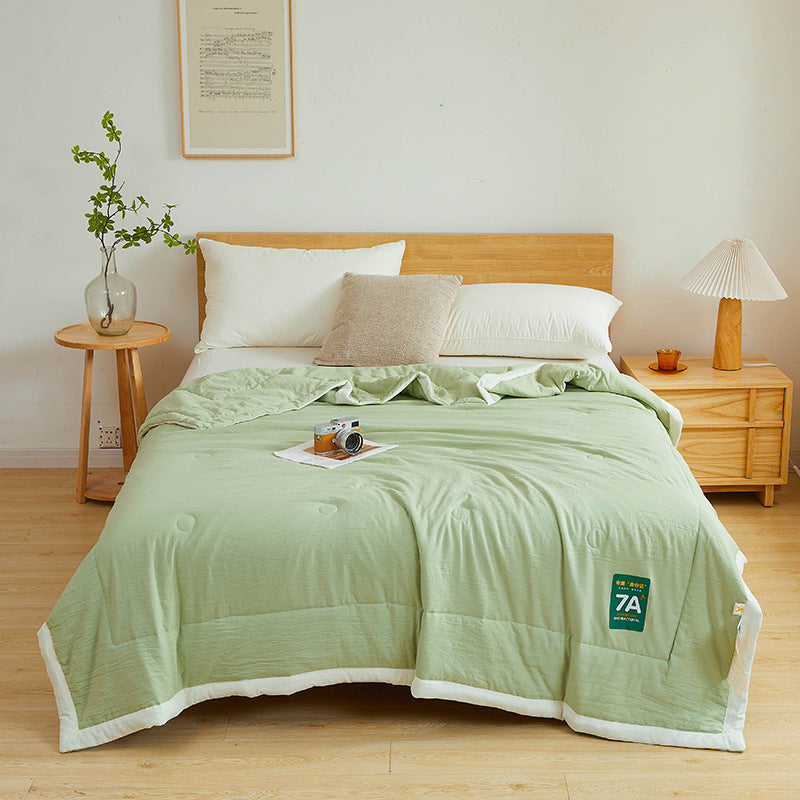Shopi Vella antibacterial summer quilt in light green on a wooden bed with neutral pillows