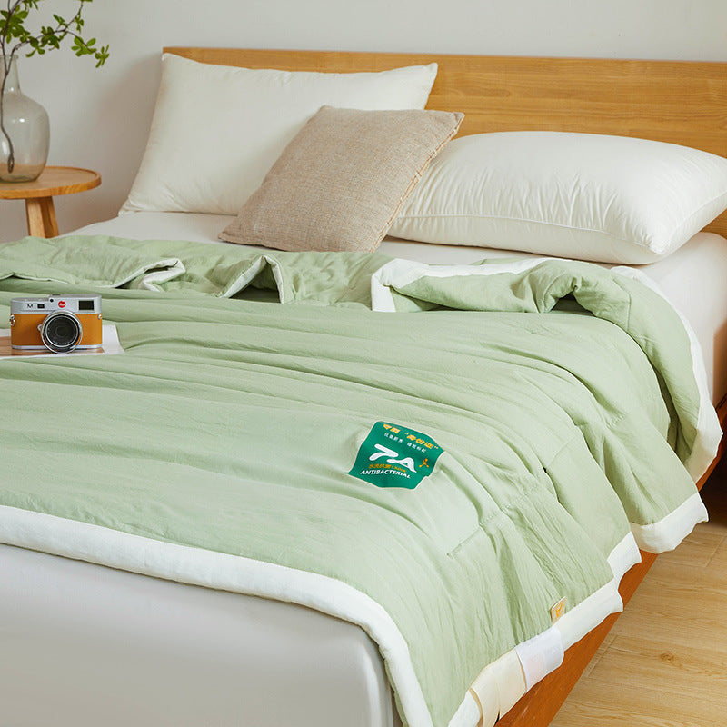 Shopi Vella antibacterial summer quilt in light green spread on bed with white pillows and beige cushion