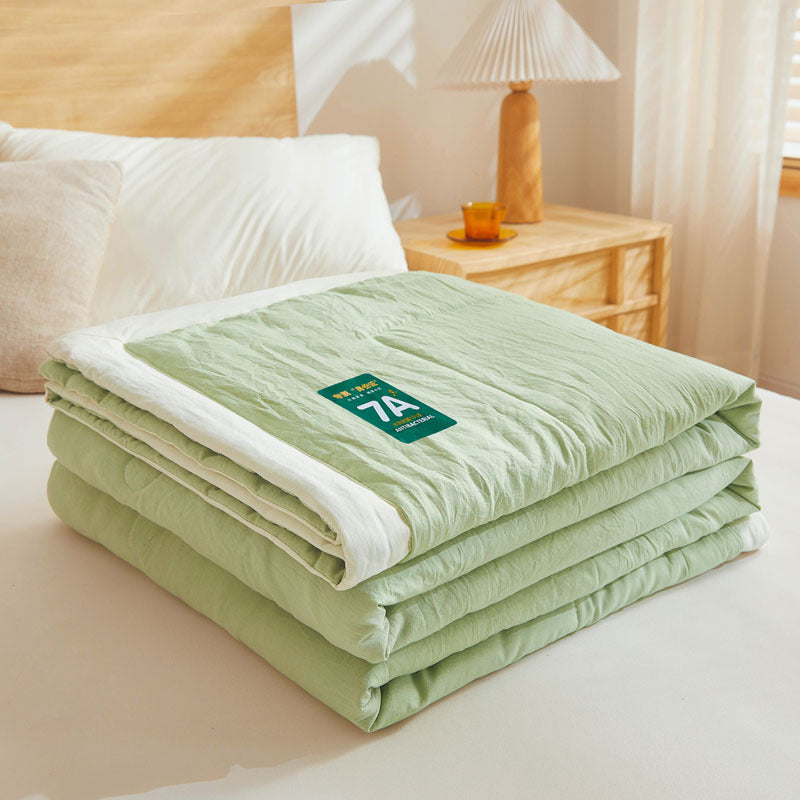 Shopi Vella antibacterial summer quilt in light green folded on bed with white trim