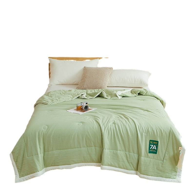 Shopi Vella antibacterial summer quilt in light green on bed with pillows and camera