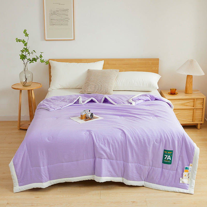 Shopi Vella antibacterial summer quilt in lavender color on a wooden bed with white pillows
