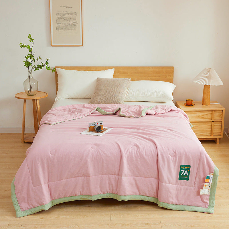 Shopi Vella antibacterial summer quilt in pink with green trim on a wooden bed in a bright bedroom
