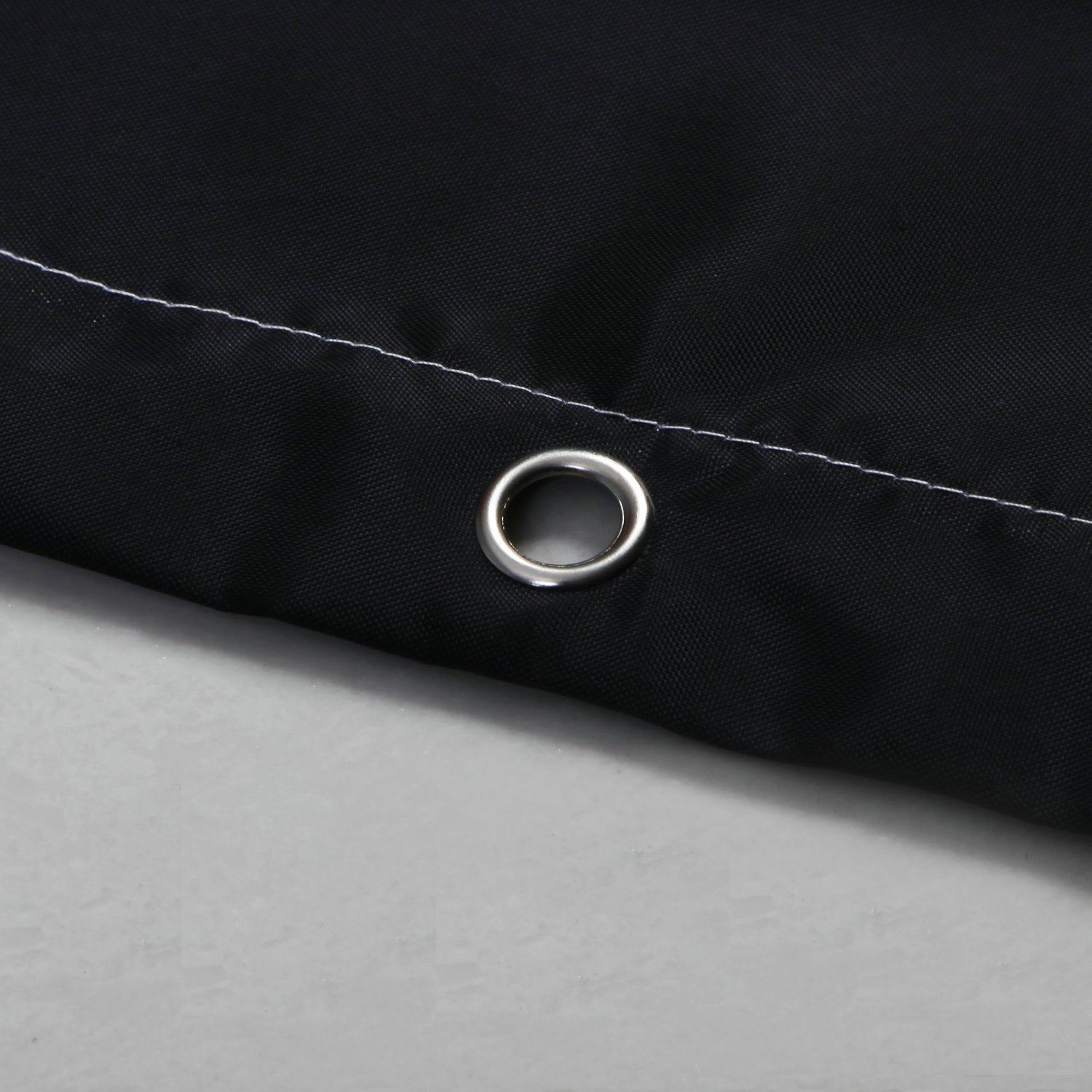 Close-up of black waterproof shower curtain corner with metal grommet and white stitching