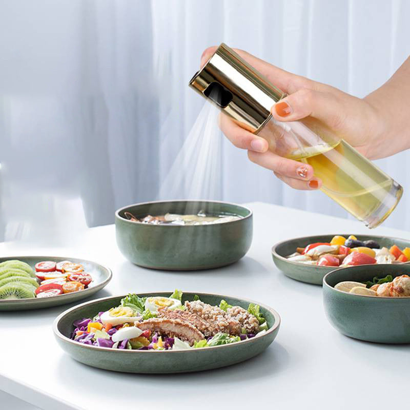 Hand spraying oil from Shopi Vella BBQ oil spray bottle onto food in green kitchen bowls