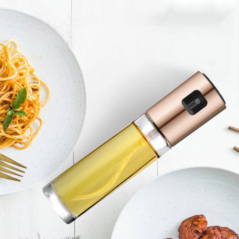 Shopi Vella BBQ oil spray bottle with clear glass body and rose gold top next to plates of pasta and grilled meat