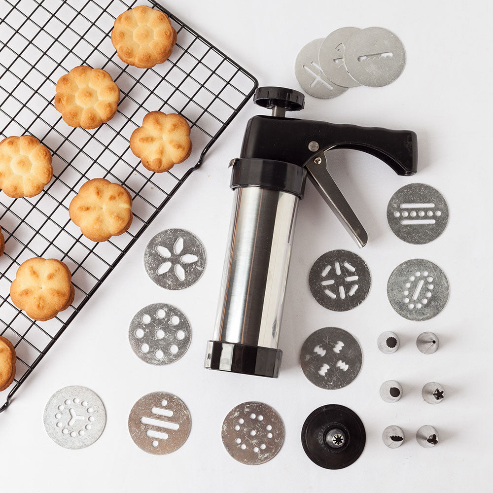 Shopi Vella biscuit press machine with multiple metal discs and freshly baked biscuits on cooling rack