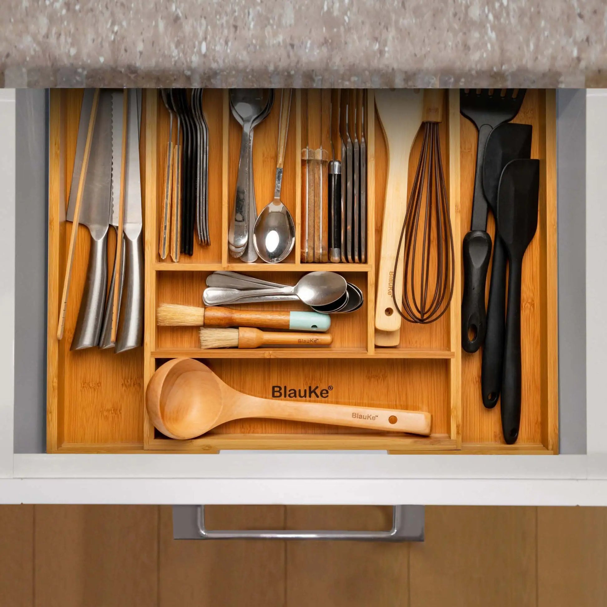 Expandable bamboo drawer organizer neatly storing kitchen utensils and cutlery in a kitchen drawer