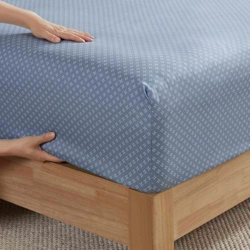 Blue floral comforter set queen fitted sheet being placed on wooden bed frame by hands