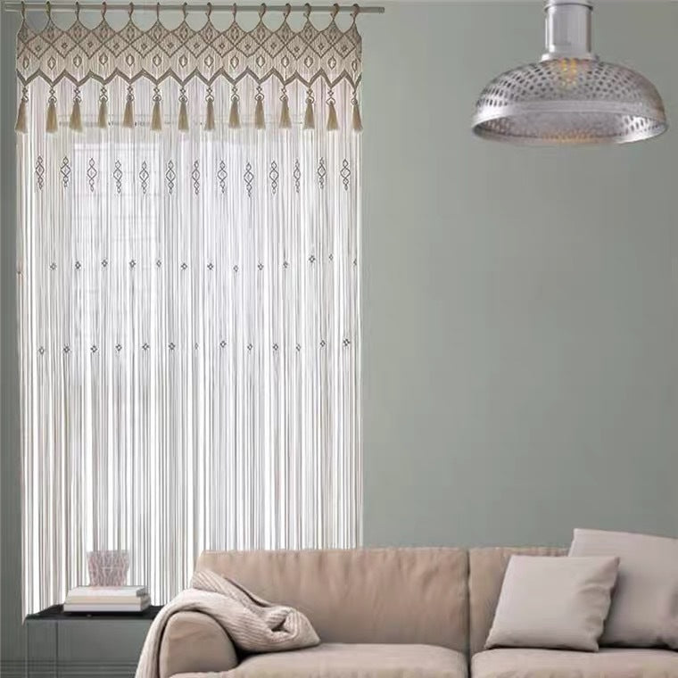 Bohemian hand woven curtain with tassels hanging in a living room with beige sofa and modern lamp