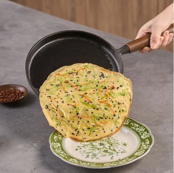Shopi Vella cast iron pizza pan with wooden handle lifting a freshly cooked pizza onto a decorative plate