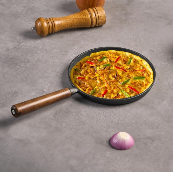Shopi Vella cast iron pizza pan with wooden handle cooking a vegetable pizza on a gray surface