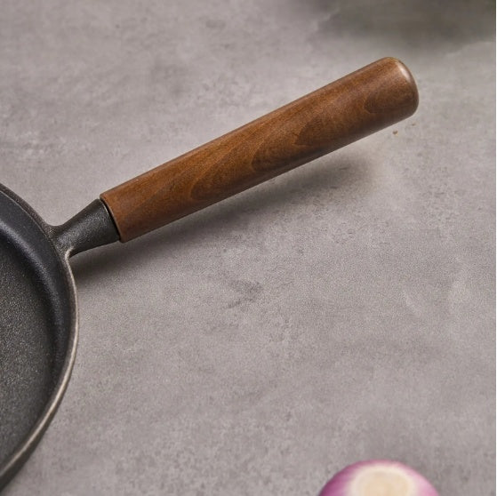 Shopi Vella cast iron pizza pan with wooden handle on gray surface next to sliced red onion