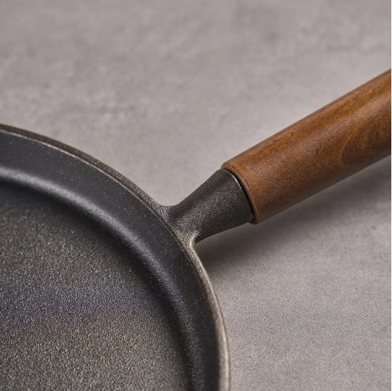 Close-up of Shopi Vella cast iron pizza pan with wooden handle on gray surface