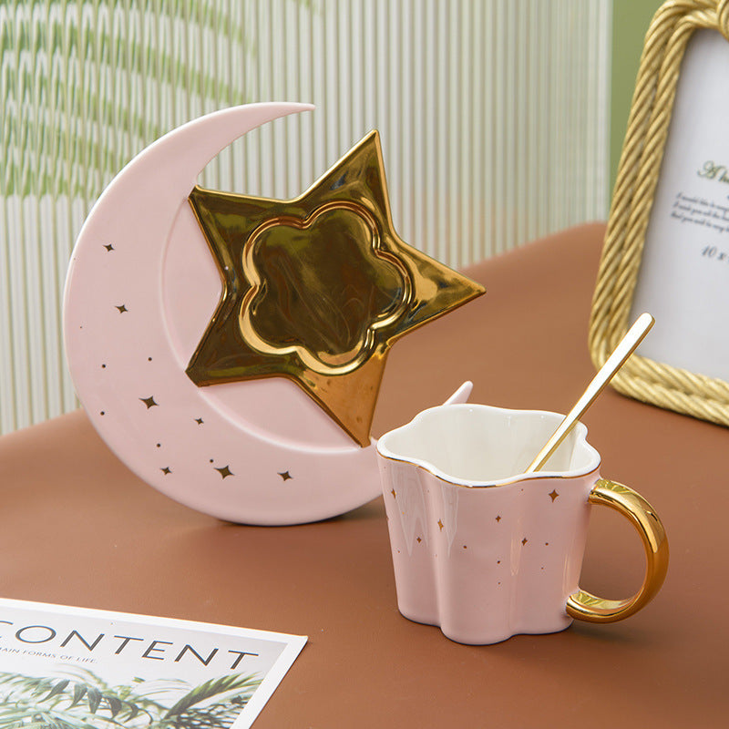 Shopi Vella ceramic cup with star and moon saucer in pink and gold with gold spoon on brown table