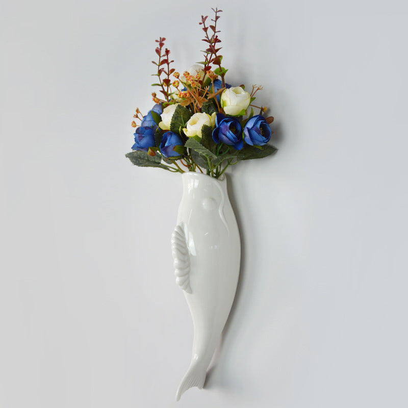 White ceramic goldfish wall vase holding artificial blue and white flowers for home storage decor