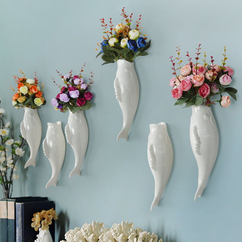 Set of ceramic goldfish wall vase holders in white with colorful artificial flowers on blue wall