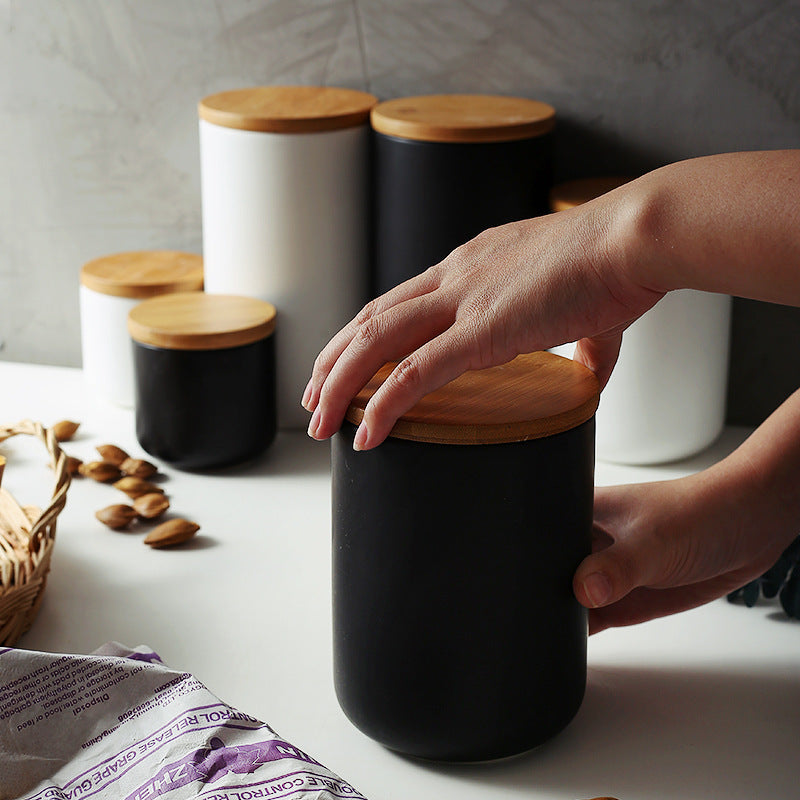 Shopi Vella ceramic kitchen storage jar in black with wooden lid held by hands on kitchen counter