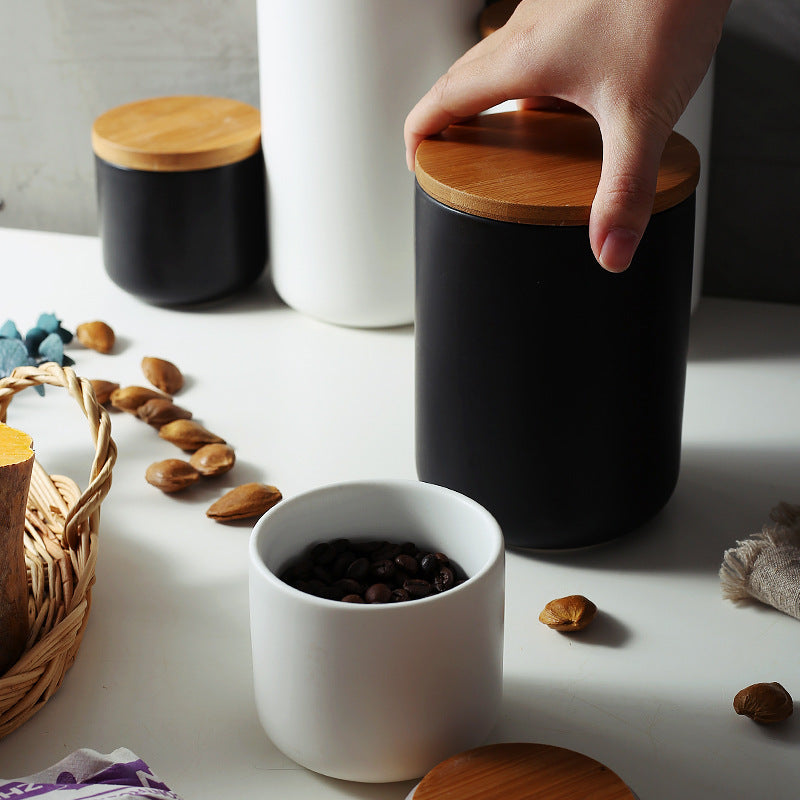 Shopi Vella ceramic kitchen storage jar with black body and wooden lid being held on white countertop