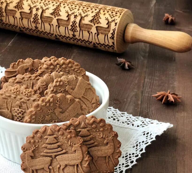 Christmas embossing rolling pin with reindeer and tree patterns next to festive embossed cookies in white bowl