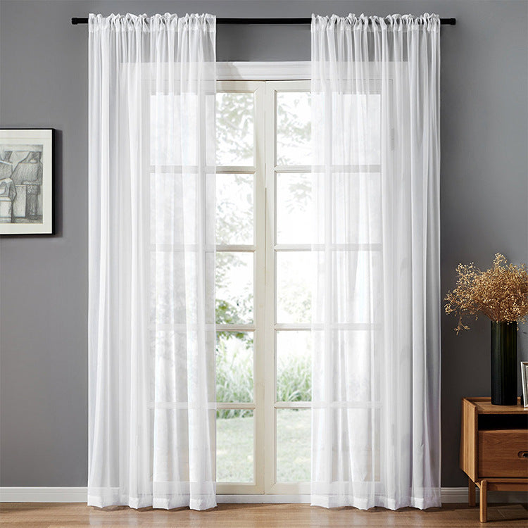 Sheer white cotton linen window curtains hanging over a glass door in a modern gray room