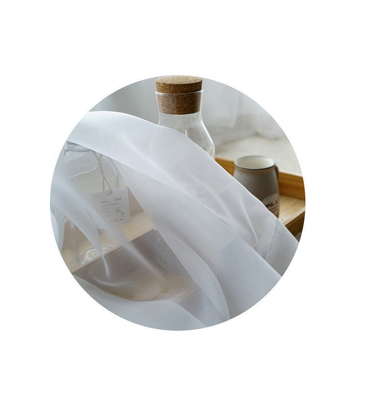 Sheer white cotton linen window curtains softly flowing beside a glass bottle and ceramic cup