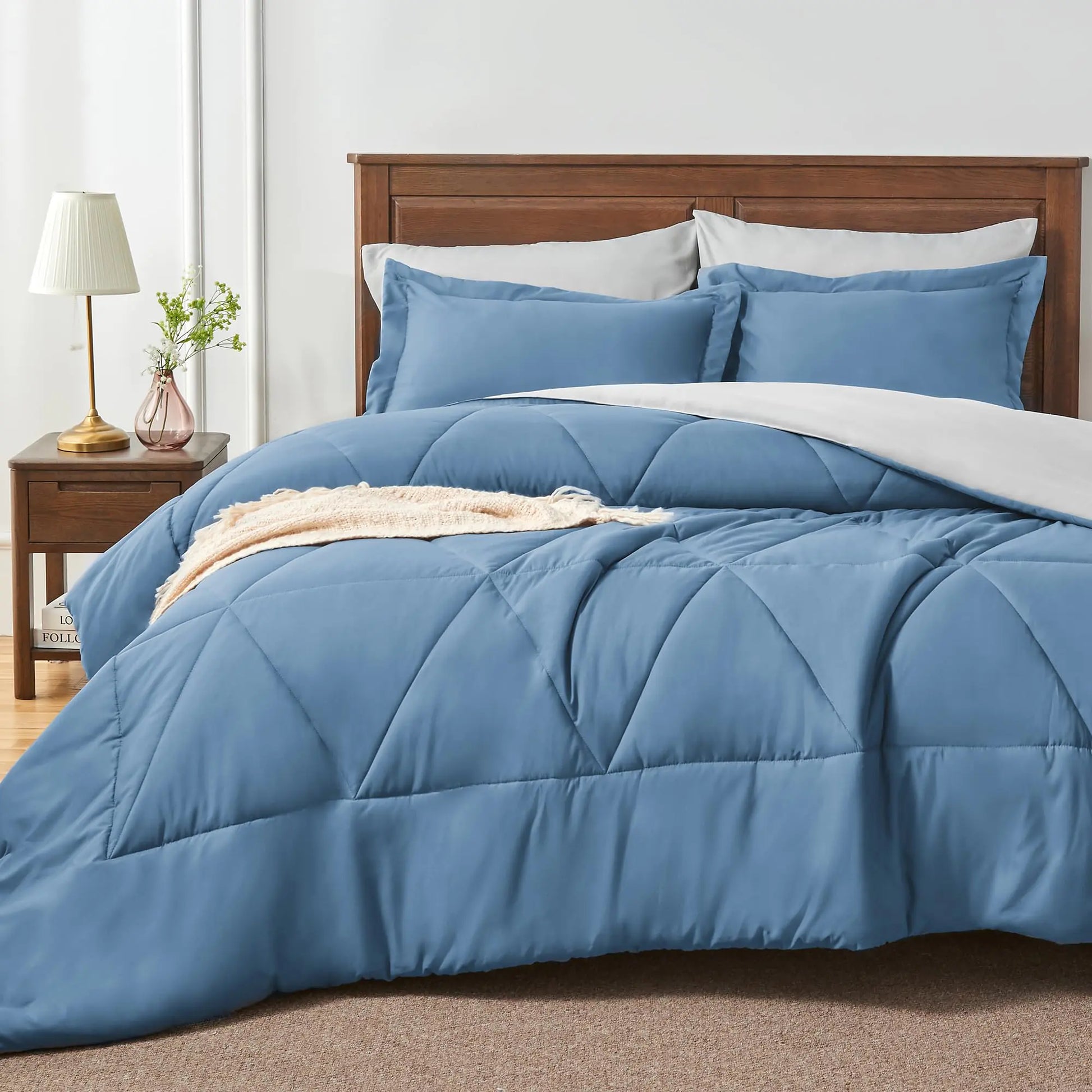 Cozy blue comforter set with sheets on bed in bedroom with wooden headboard and nightstand