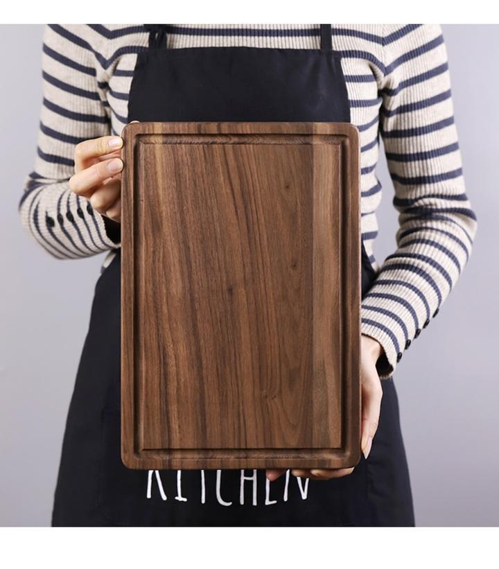Person holding a creative wood cutting board for kitchen made of dark polished wood with juice groove