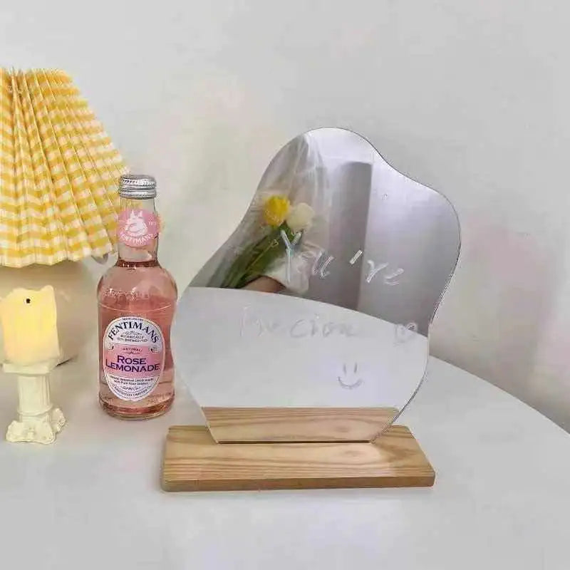 Irregular shaped dorm decor vanity mirror with wooden base placed on white table next to lemonade bottle and lamp