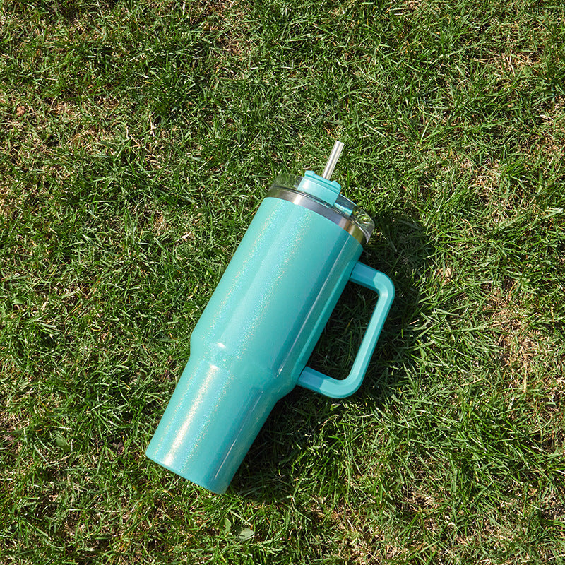 Shopi Vella double-layer stainless steel cup in teal with handle and metal straw on grass