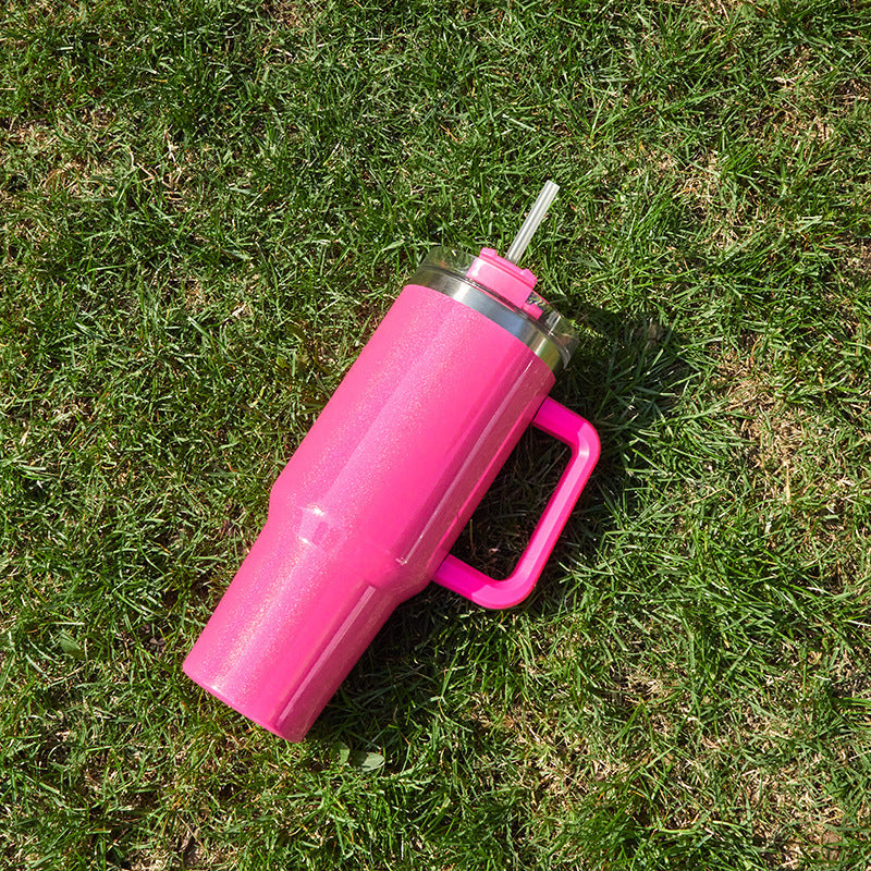Pink double-layer stainless steel cup with handle and straw on green grass by Shopi Vella