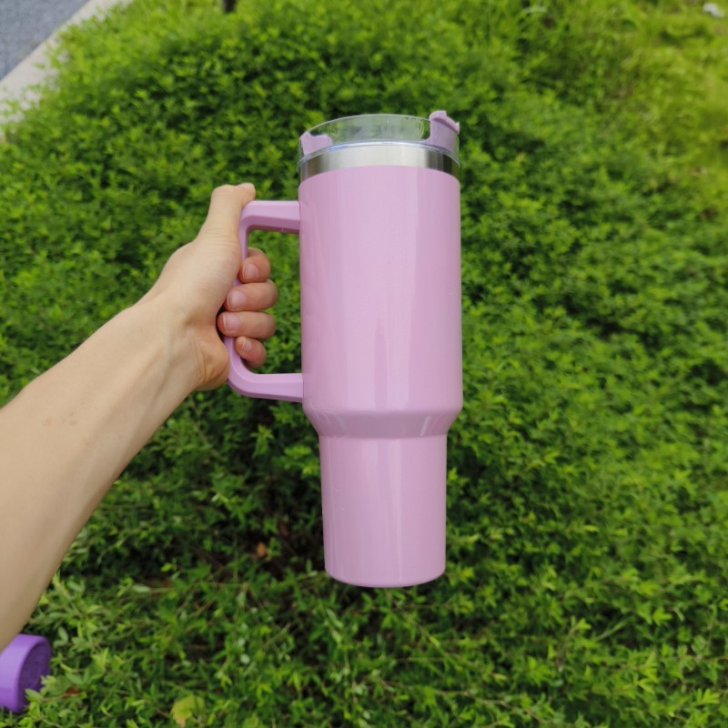 Pink double-layer stainless steel cup with handle held against green foliage background