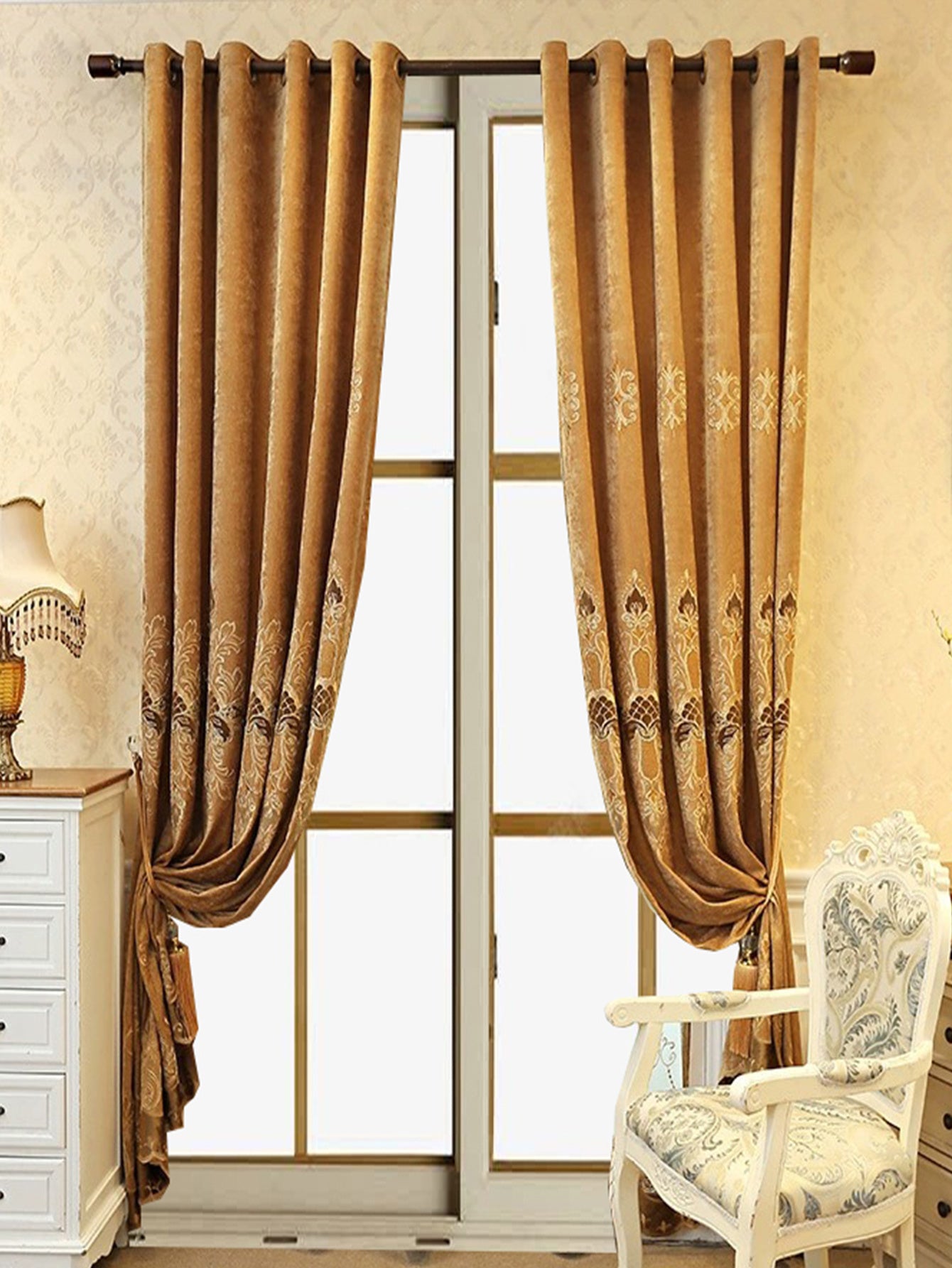Elegant blackout curtains in gold with intricate patterns hanging by a window with decorative furniture nearby