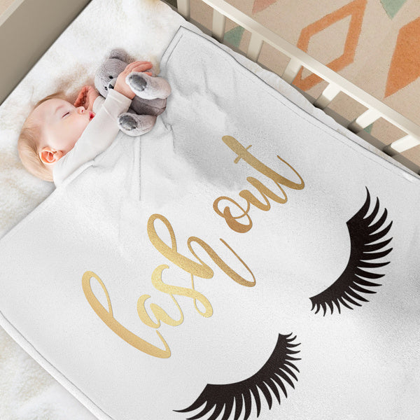 Shopi Vella eyelash print throw blanket with gold script and black lashes on a baby in crib