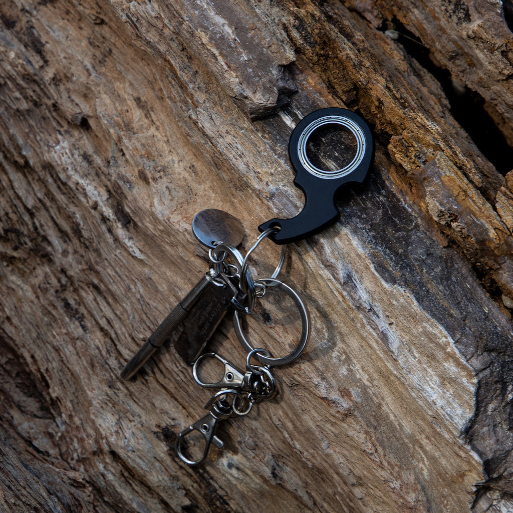 Shopi Vella black finger spinner bottle opener keychain on textured wooden surface