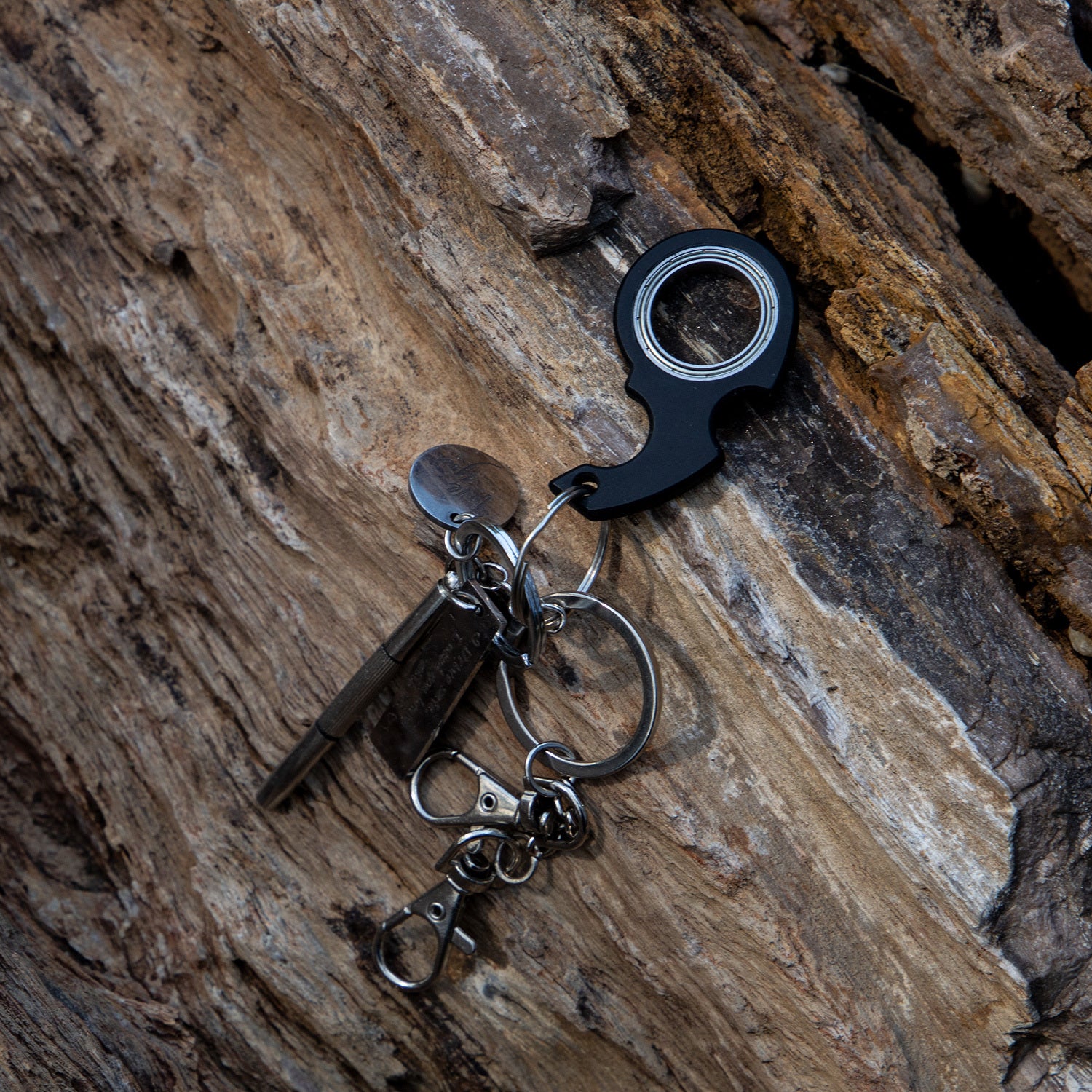 Shopi Vella black finger spinner bottle opener keychain on textured wooden surface