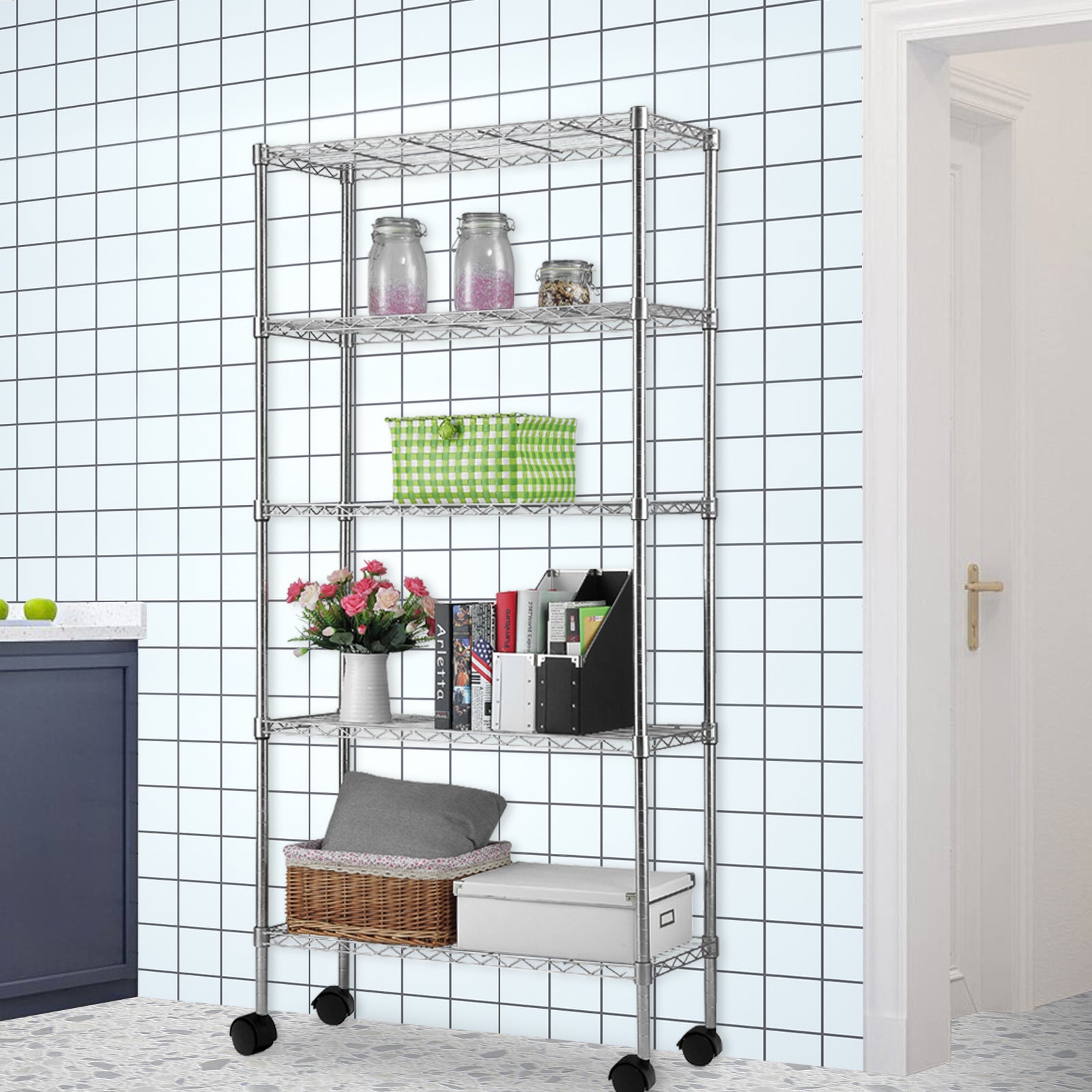 Shopi Vella five tier metal storage rack with wheels holding jars, a basket, and books against tiled wall