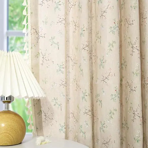 Beige floral farmhouse curtains with delicate botanical print hanging beside a wooden lamp on a white table