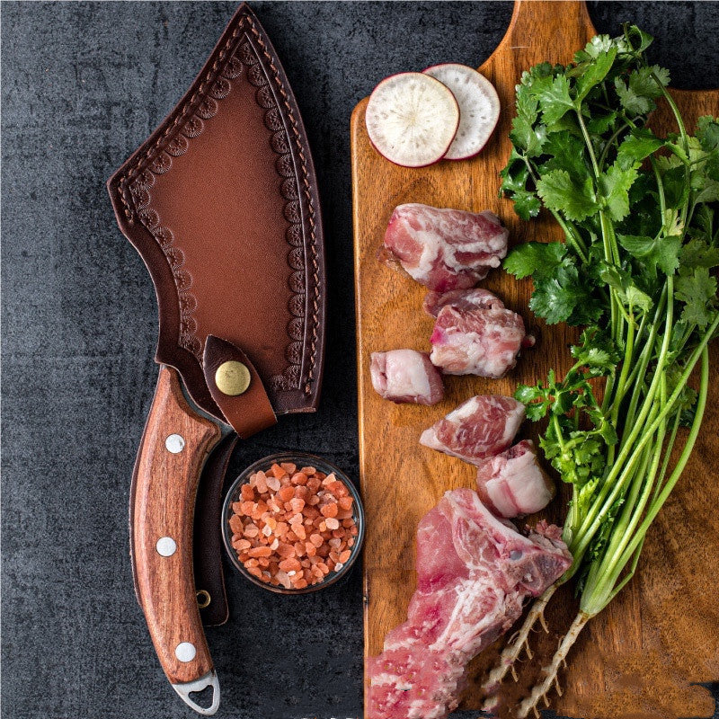 Forged small kitchen knife with wooden handle and leather sheath next to fresh herbs and meat on cutting board