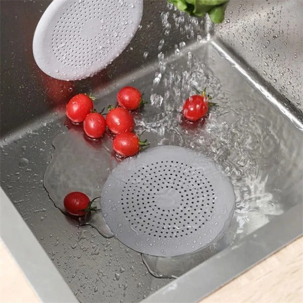 Shopi Vella kitchen sink hair filter placed in stainless steel sink with running water and cherry tomatoes